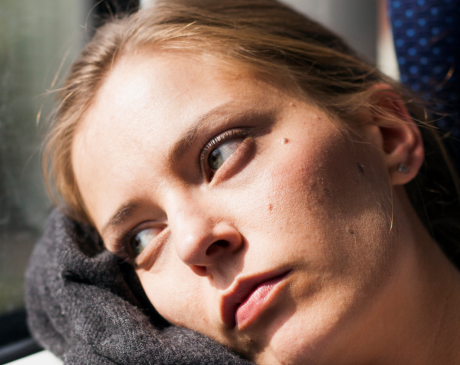 Woman sitting on a train, leaning her head against the window while staring outside. 